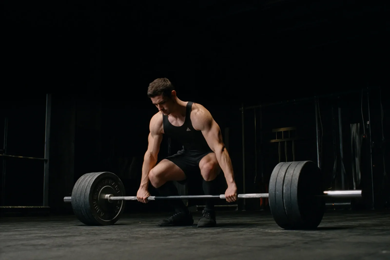 An athlete sets up a barbell deadlift in a dark training space